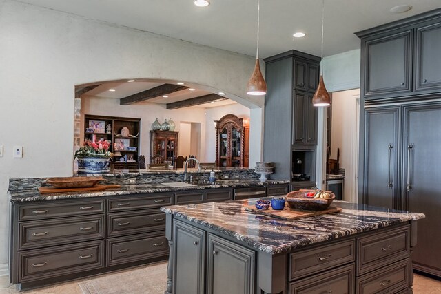 kitchen featuring a sink, arched walkways, dark stone countertops, recessed lighting, and paneled fridge
