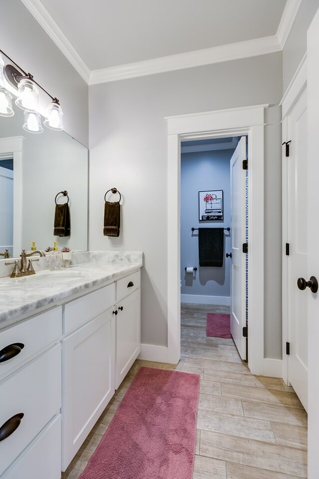 bathroom featuring baseboards, ornamental molding, vanity, and wood finished floors