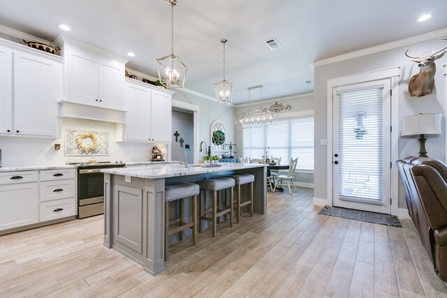 kitchen featuring a kitchen breakfast bar, a center island with sink, stainless steel range with electric cooktop, visible vents, and crown molding