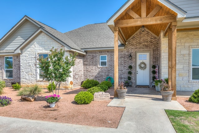 doorway to property featuring stone siding, a shingled roof, and brick siding