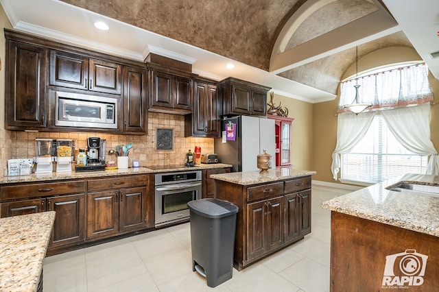 kitchen with lofted ceiling, dark brown cabinetry, decorative light fixtures, appliances with stainless steel finishes, and light stone countertops