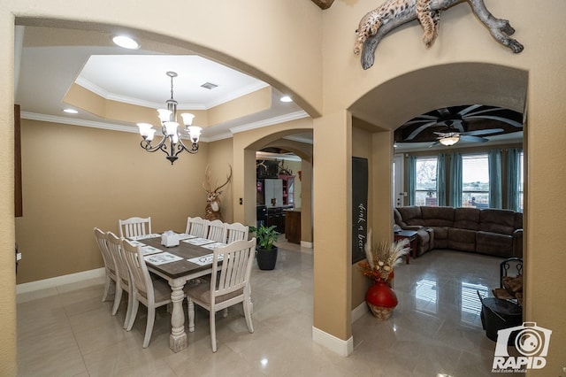 tiled dining area featuring ornamental molding, ceiling fan with notable chandelier, and a tray ceiling