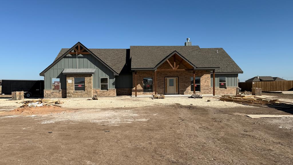 view of front facade featuring a shingled roof, fence, board and batten siding, and brick siding