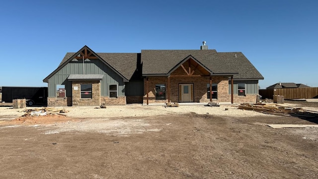 view of front facade featuring a shingled roof, fence, board and batten siding, and brick siding