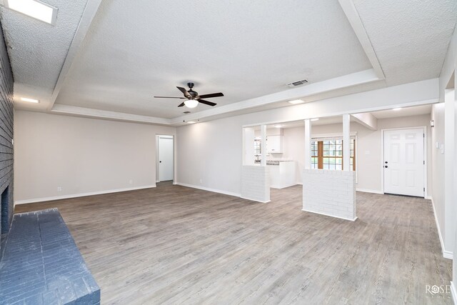 unfurnished living room with wood-type flooring, a raised ceiling, a brick fireplace, and a textured ceiling