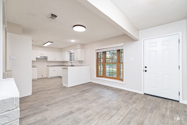 kitchen featuring sink, white cabinetry, beam ceiling, light hardwood / wood-style floors, and a textured ceiling