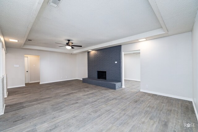 unfurnished living room featuring a raised ceiling, wood-type flooring, a brick fireplace, and a textured ceiling