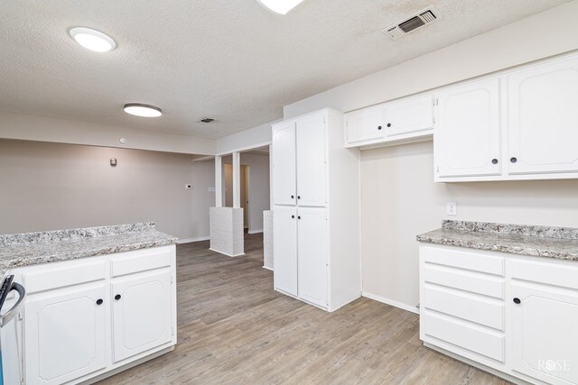 kitchen featuring white cabinetry, a textured ceiling, light wood-type flooring, light stone countertops, and stove