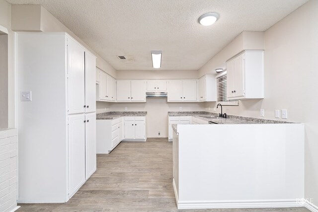 kitchen with sink, white cabinets, a textured ceiling, and light hardwood / wood-style floors