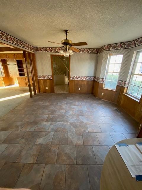 unfurnished room featuring ceiling fan, a textured ceiling, and wood walls