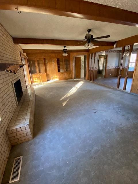 unfurnished living room with a brick fireplace, beam ceiling, ceiling fan, and brick wall