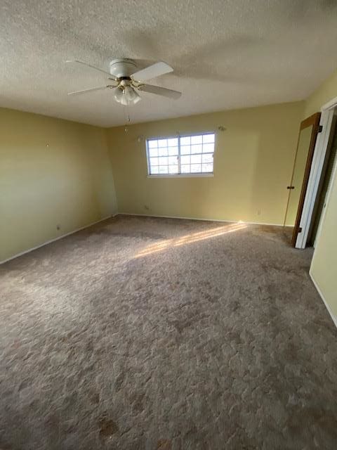 spare room with ceiling fan, dark carpet, and a textured ceiling