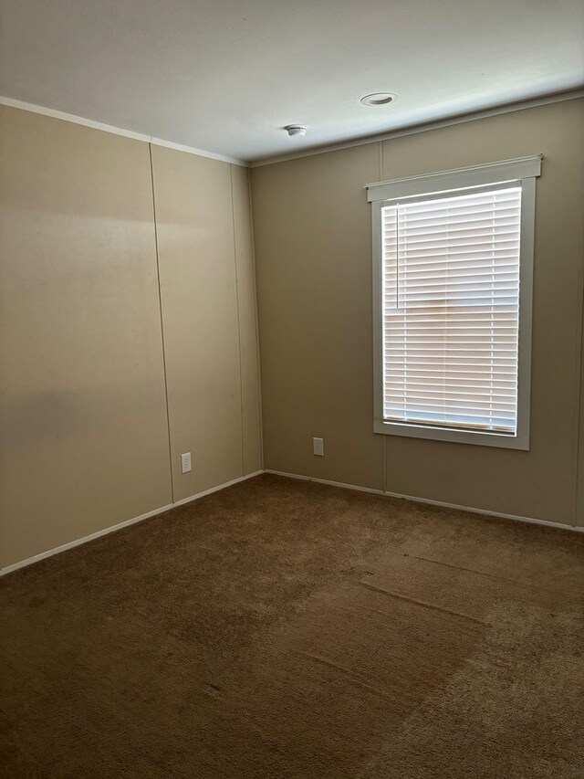 empty room with ornamental molding and dark carpet