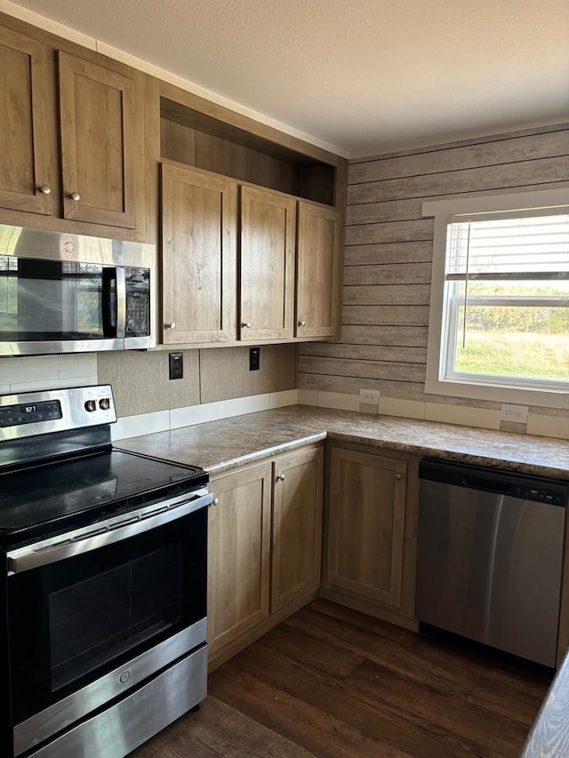 kitchen with appliances with stainless steel finishes, wooden walls, and dark hardwood / wood-style flooring