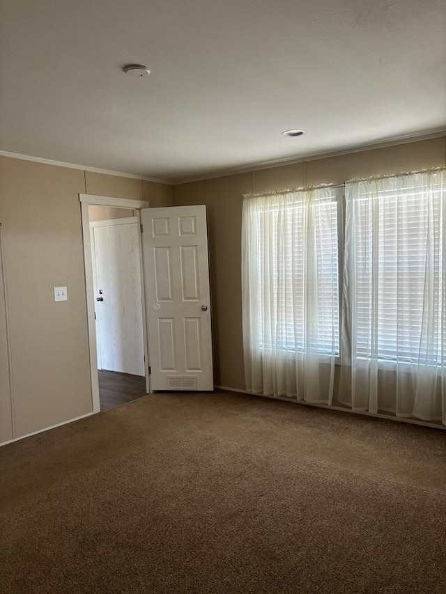 unfurnished room with ornamental molding and dark colored carpet