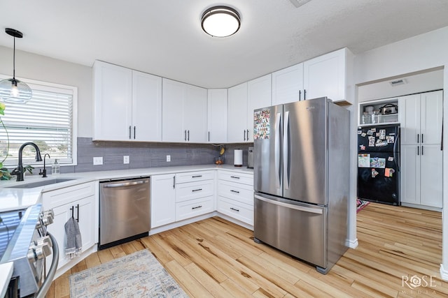 kitchen featuring appliances with stainless steel finishes, sink, white cabinets, and decorative light fixtures