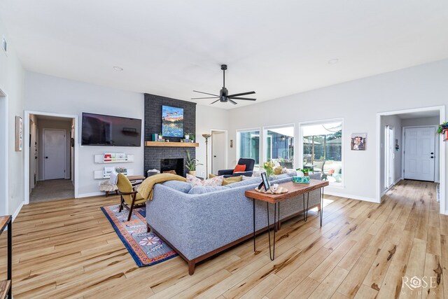 living room with ceiling fan, a brick fireplace, and light hardwood / wood-style floors