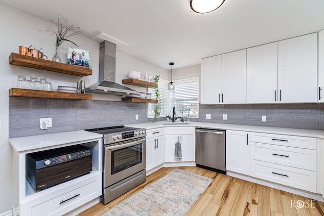 kitchen featuring sink, appliances with stainless steel finishes, white cabinetry, hanging light fixtures, and wall chimney exhaust hood