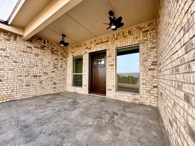 entrance to property with a ceiling fan, a patio area, and brick siding