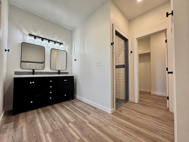 full bathroom featuring double vanity, baseboards, a walk in closet, and wood finished floors