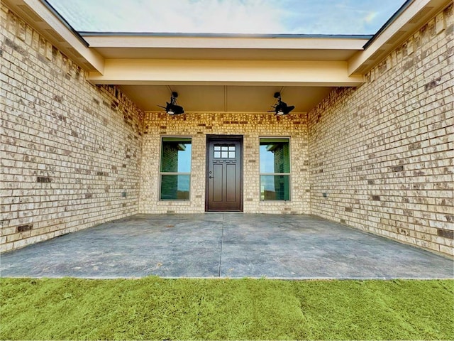 view of exterior entry with ceiling fan, a patio, and brick siding