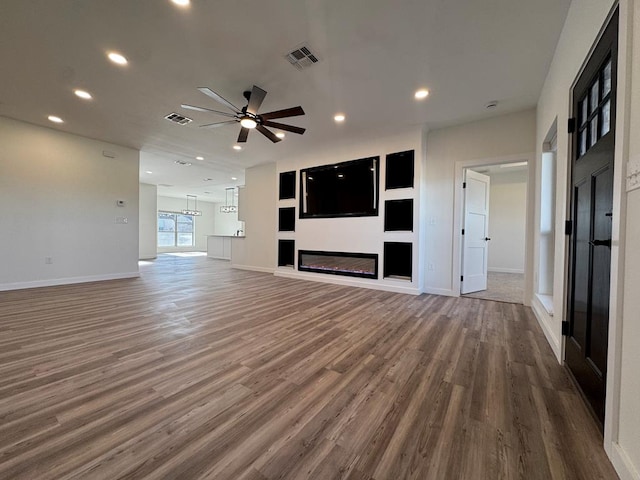 unfurnished living room with ceiling fan, visible vents, dark wood-style flooring, and a glass covered fireplace