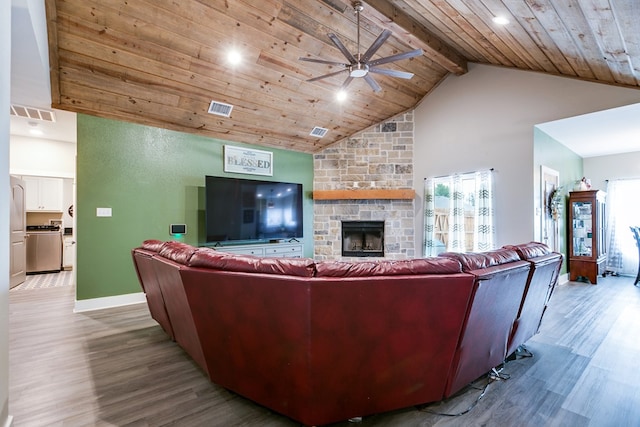 living room featuring wood ceiling, a stone fireplace, light hardwood / wood-style floors, and beamed ceiling