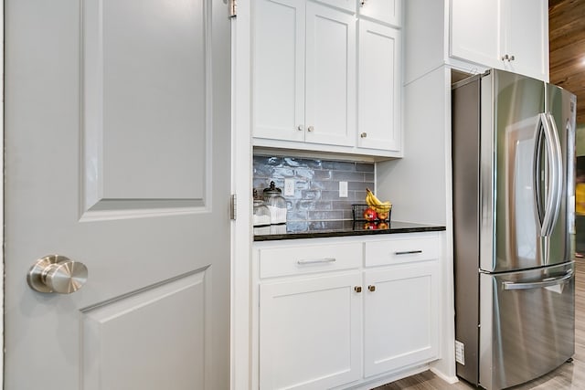 kitchen featuring stainless steel refrigerator, dark stone counters, backsplash, and white cabinets