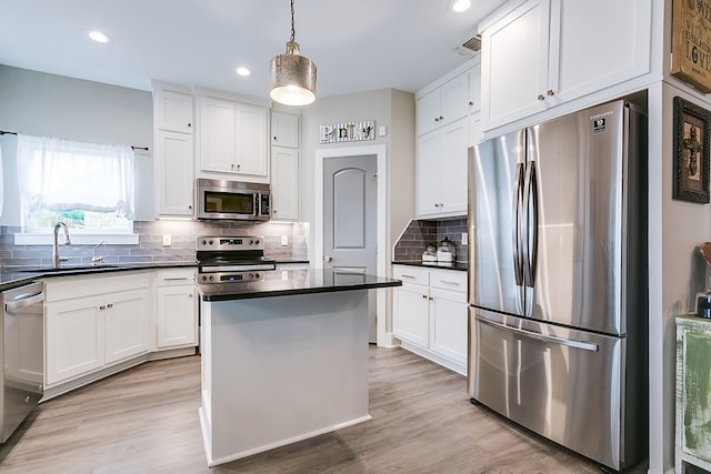 kitchen with light wood-type flooring, dark countertops, appliances with stainless steel finishes, and white cabinetry