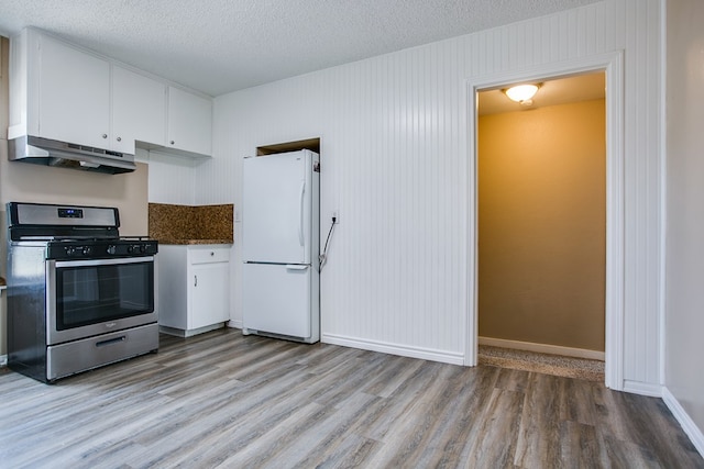 1619 Spaulding St, San Angelo, TX 76905 - kitchen featuring stainless steel range with gas stovetop, freestanding refrigerator, under cabinet range hood, light wood-type flooring, and white cabinets