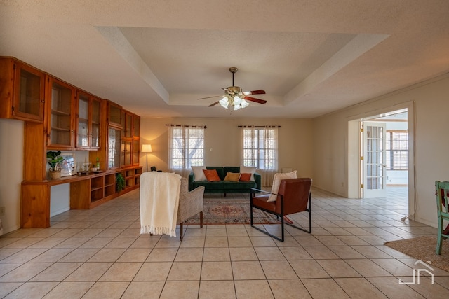 living room with ceiling fan, a tray ceiling, a textured ceiling, and light tile patterned floors