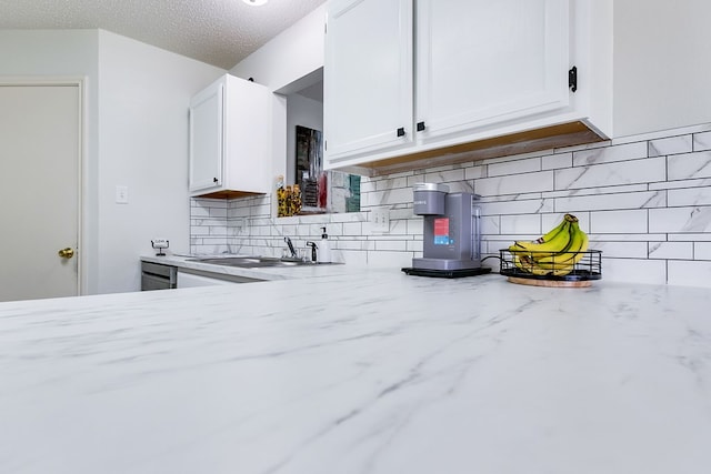 kitchen with a sink, white cabinets, light stone counters, and decorative backsplash