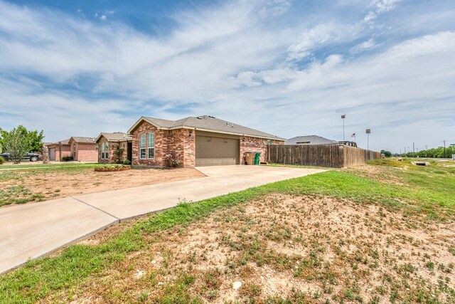 view of front facade with brick siding, an attached garage, concrete driveway, and fence