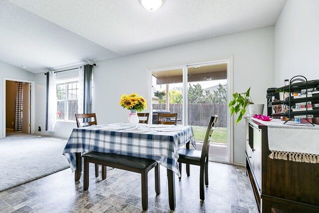 dining area with stone finish flooring, a textured ceiling, and vaulted ceiling