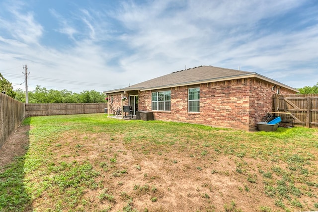 rear view of property featuring a shingled roof, a lawn, central AC, brick siding, and a fenced backyard