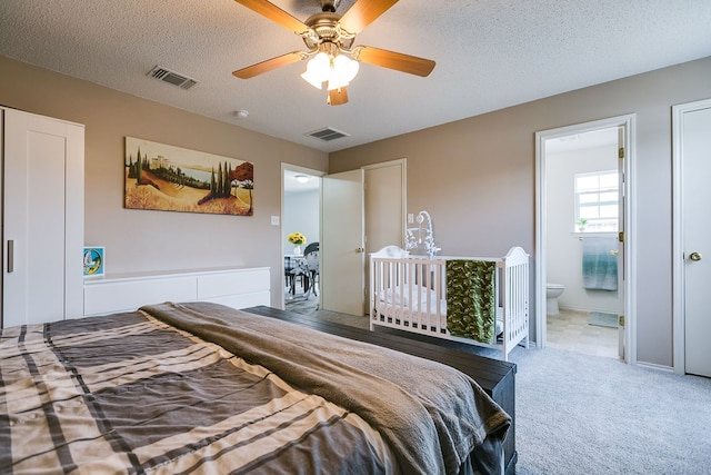carpeted bedroom with a textured ceiling, visible vents, ceiling fan, and ensuite bath