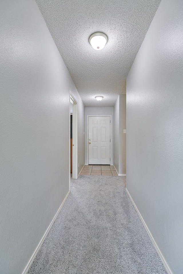 corridor with light tile patterned floors, a textured ceiling, light carpet, and baseboards