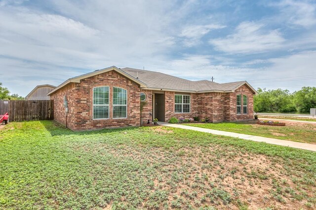 ranch-style house with a front lawn, roof with shingles, brick siding, and fence