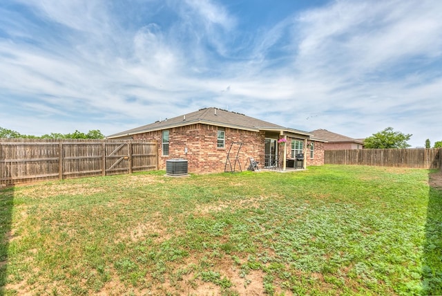 back of property with a lawn, brick siding, a fenced backyard, and central air condition unit