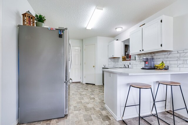 kitchen featuring a peninsula, white cabinets, freestanding refrigerator, and backsplash