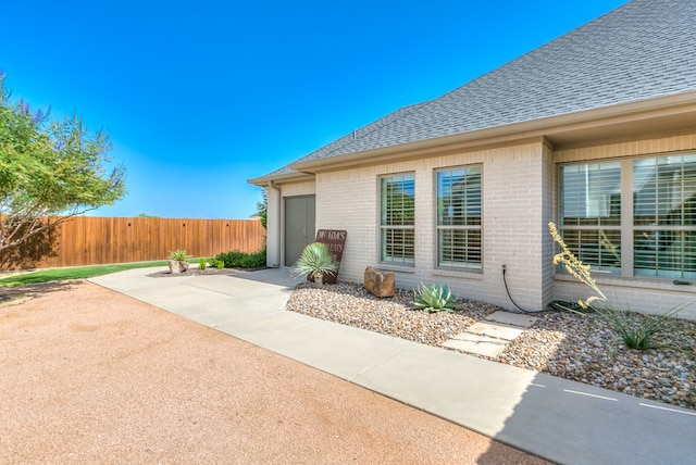 exterior space featuring brick siding, a patio, roof with shingles, and fence