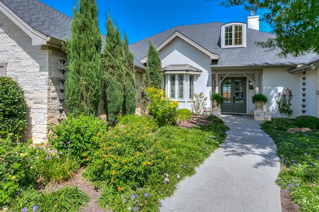 property entrance featuring stucco siding, stone siding, french doors, a shingled roof, and a chimney