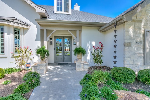 property entrance with stucco siding, stone siding, a chimney, and a shingled roof