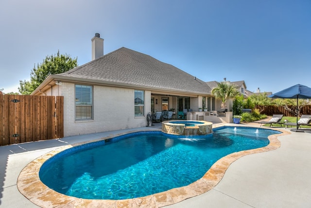 view of pool featuring fence, a pool with connected hot tub, an outdoor kitchen, and a patio area