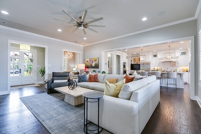 living area with dark wood-type flooring, recessed lighting, ceiling fan with notable chandelier, and ornamental molding