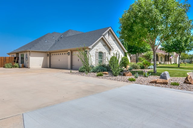 view of front of home featuring fence, roof with shingles, a garage, stone siding, and driveway