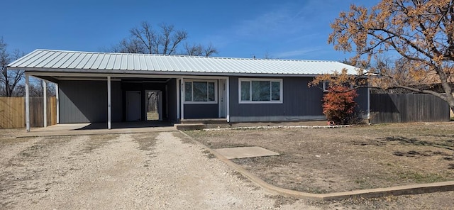 single story home with dirt driveway, fence, metal roof, and a carport