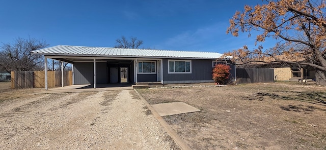 ranch-style house with metal roof, dirt driveway, fence, and an attached carport