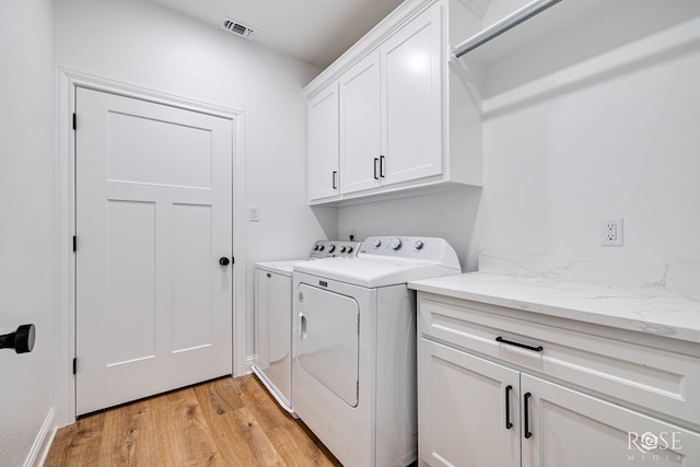 laundry room with independent washer and dryer, cabinets, and light wood-type flooring