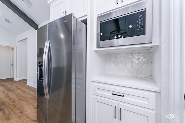 kitchen featuring appliances with stainless steel finishes, hardwood / wood-style floors, white cabinets, and decorative backsplash